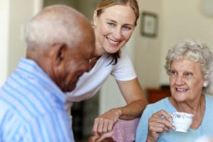 Happy female caretaker with senior people having coffee in nursing home